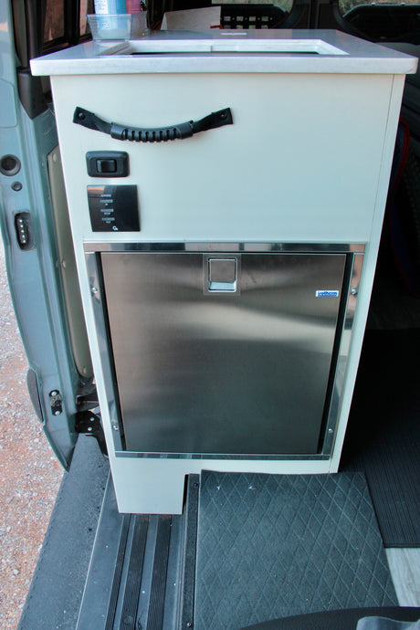 Inside this RV rental: A compact, light-colored cabinet houses a sink, Isotherm fridge, and awning controls.