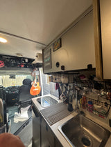 Inside an RV rental, showing the cozy kitchen with sink, stovetop, and clever storage solutions. Guitar hangs near the cab.