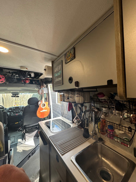 Inside an RV rental, showing the cozy kitchen with sink, stovetop, and clever storage solutions. Guitar hangs near the cab.
