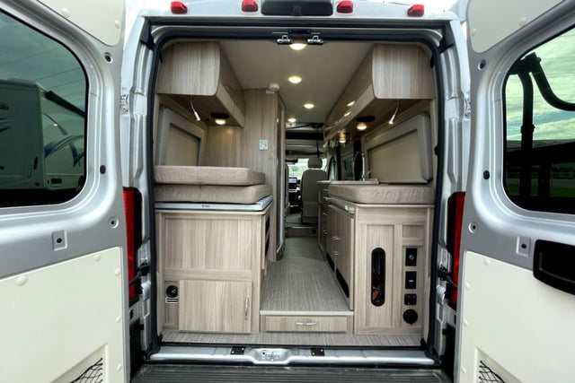  parked amidst tall forest trees.|Silver pop-top camper van (RV rental) parked in a sunny forest clearing