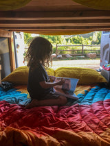 Child reads in a colorful RV rental bed, enjoying van life with open views of nature.