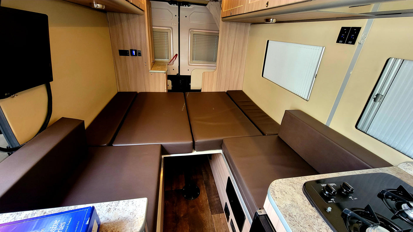 An RV rental's versatile interior with brown cushion seating that converts to a bed, a TV, and a compact kitchen.