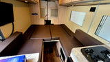 An RV rental's versatile interior with brown cushion seating that converts to a bed, a TV, and a compact kitchen.