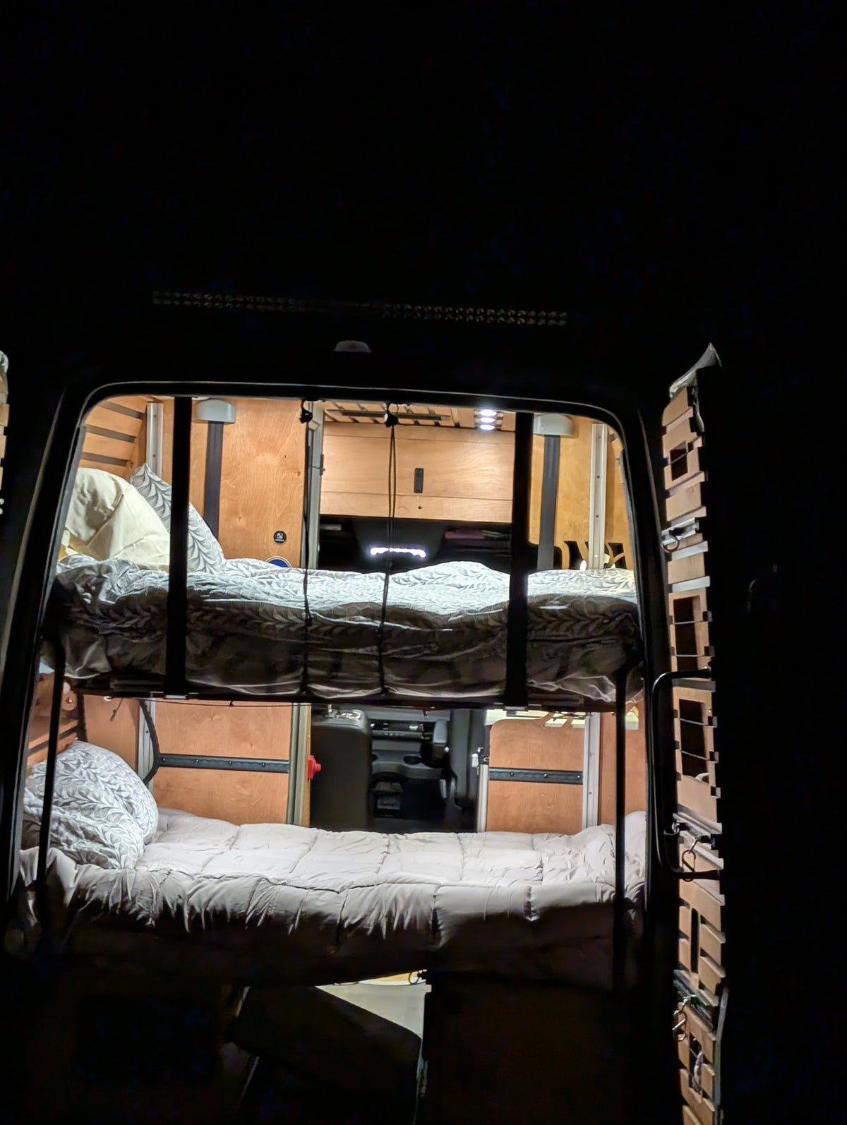 Cozy RV rental interior at night: illuminated bunk beds seen from the rear, inside a camper van. — photo 19
