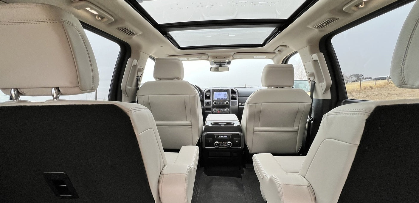 Spacious RV rental interior: Light leather seats, panoramic roof, and rear console, viewed from the 3rd row.