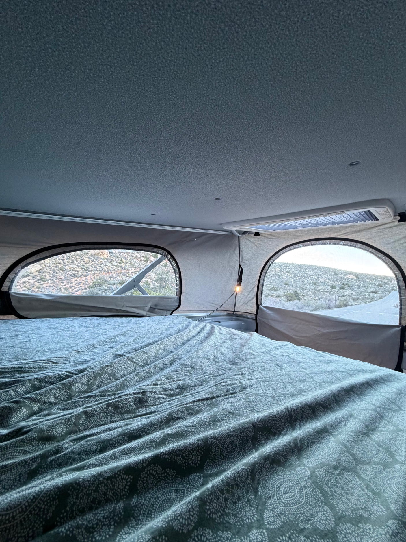 Cozy RV rental pop-top bed with desert views from arched windows, perfect for travel in a camper van.
