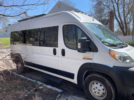 Spacious white Ram ProMaster van with large side windows and roof rack, perfect as an RV rental.