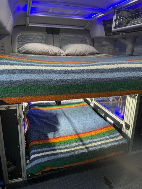 Cozy bunk beds in an RV rental, featuring colorful striped blankets & blue ambient lighting. Perfect for road trips!