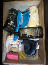 Organized RV rental cleaning kit: multi-surface wipes, dish soap, paper towels, brush, sponge, and gloves in a wooden box.