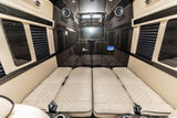 Luxurious RV rental interior with cream quilted beds, dark wood paneling, TV, and speakers for ultimate travel comfort.
