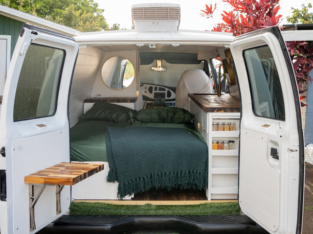 Inside an RV rental camper van: a bed with green bedding, wooden counter kitchen, and folding table. Ready for adventures.