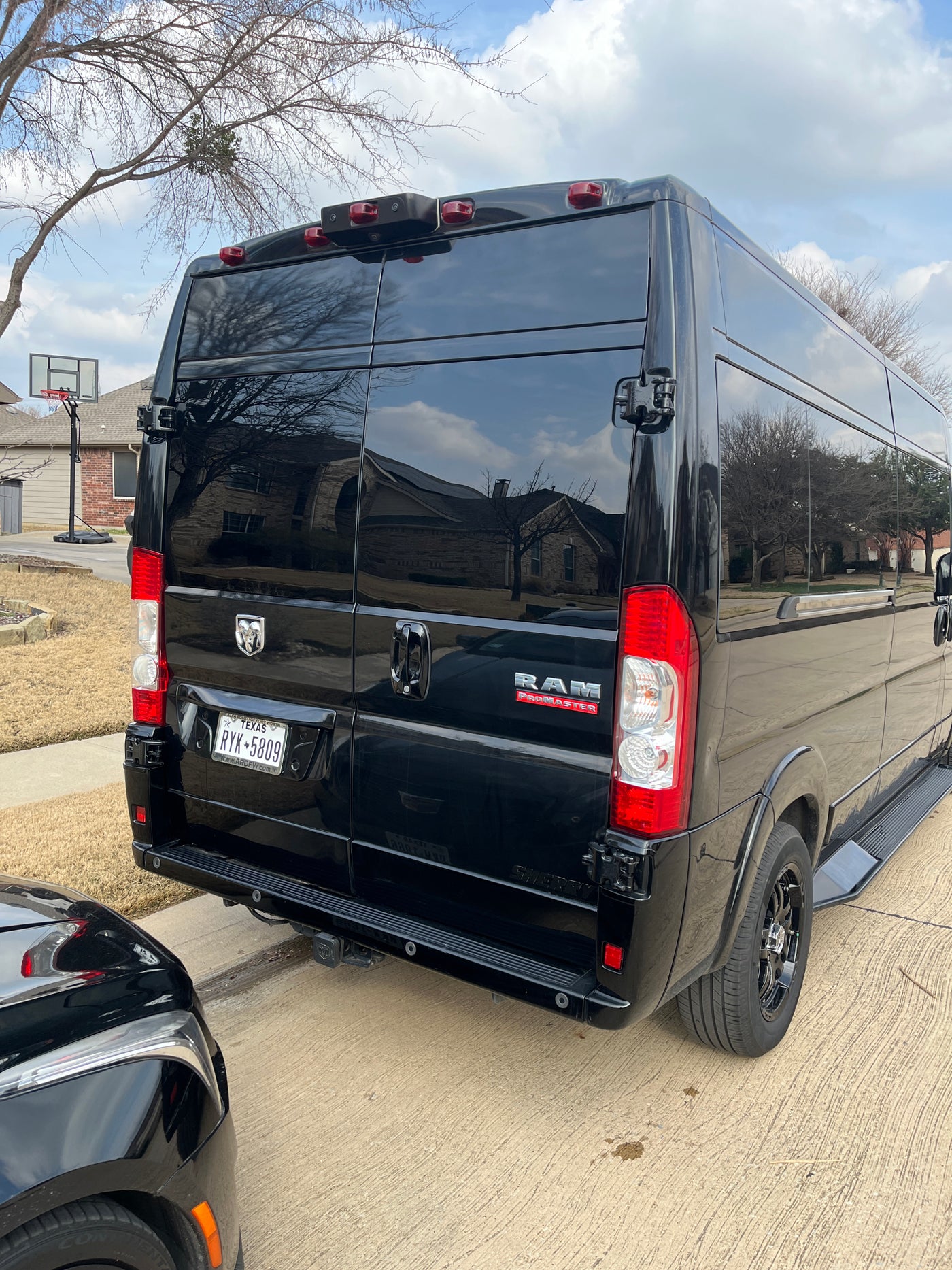 Rear view of a black Ram ProMaster RV rental van with Texas plates, parked in front of a house on a sunny day. — photo 11