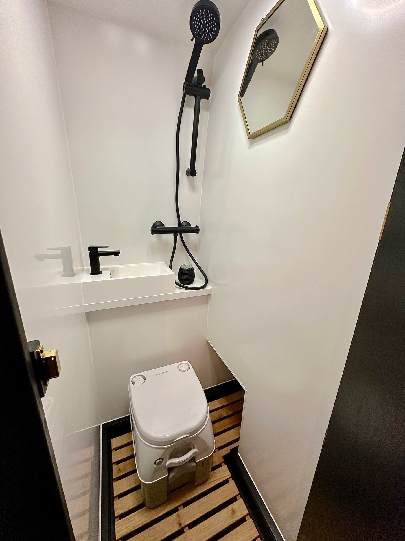 Modern RV rental bathroom with black shower, sink, Dometic toilet, wood slat floor, and hexagonal mirror. — photo 5