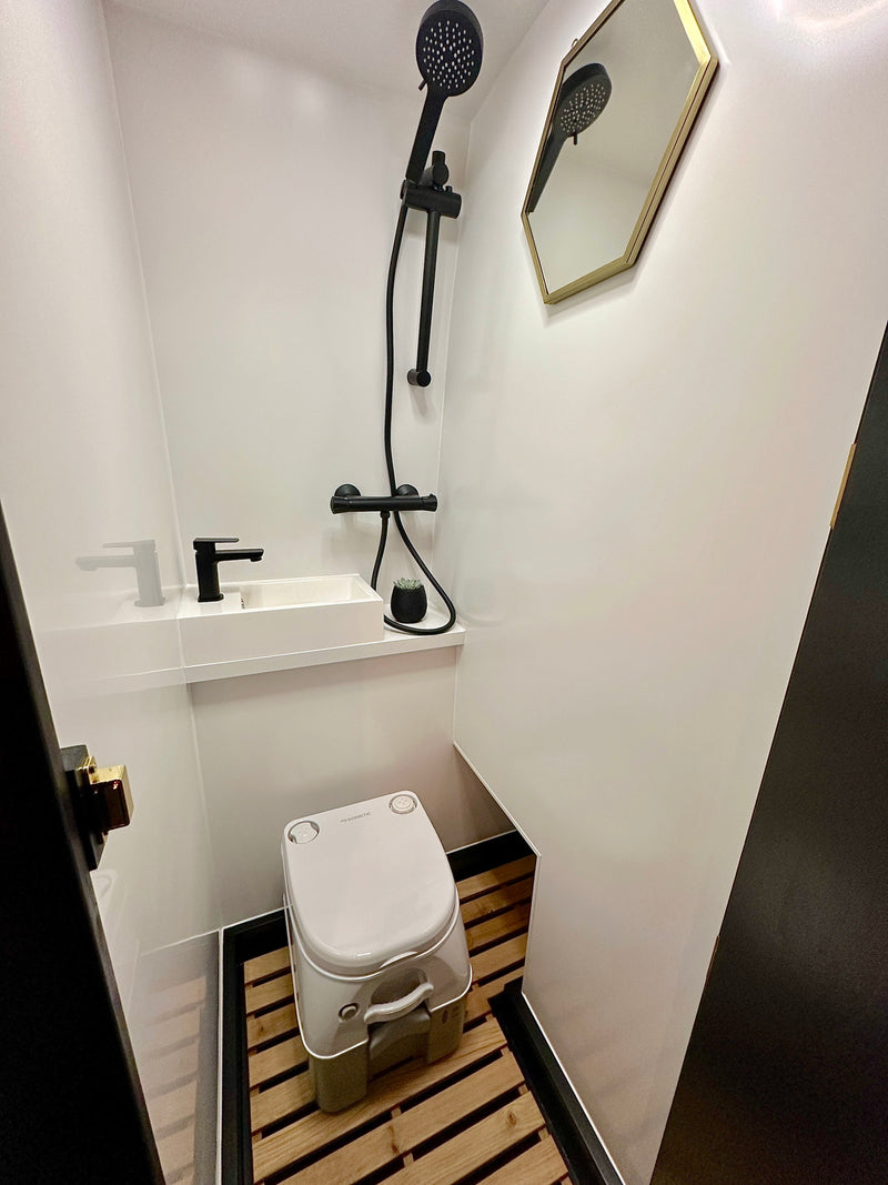 Modern RV rental bathroom with black shower, sink, Dometic toilet, wood slat floor, and hexagonal mirror. — photo 5