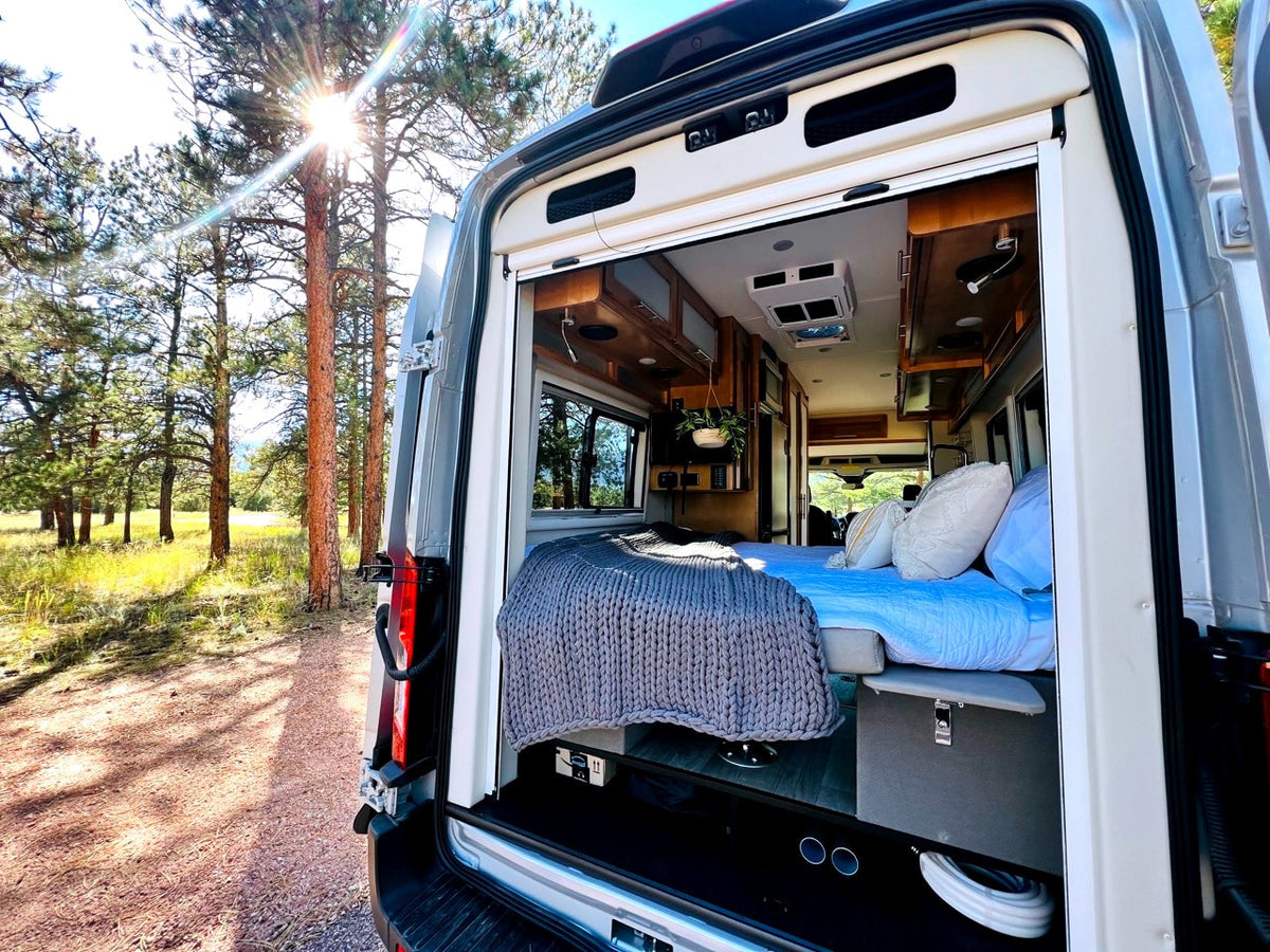 Relaxing RV rental adventure! Cozy campervan interior opens to nature, sun shining through pine trees. — photo 4