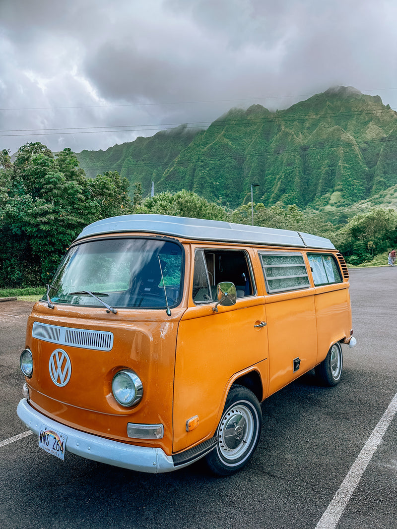 Orange vintage VW camper van (RV rental) parked in Hawaii, with lush green, cloud-covered mountains. — photo 4