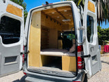 Custom wood interior of a camper van, ideal for rv rental or adventure. Features bed, storage, and cozy setup.