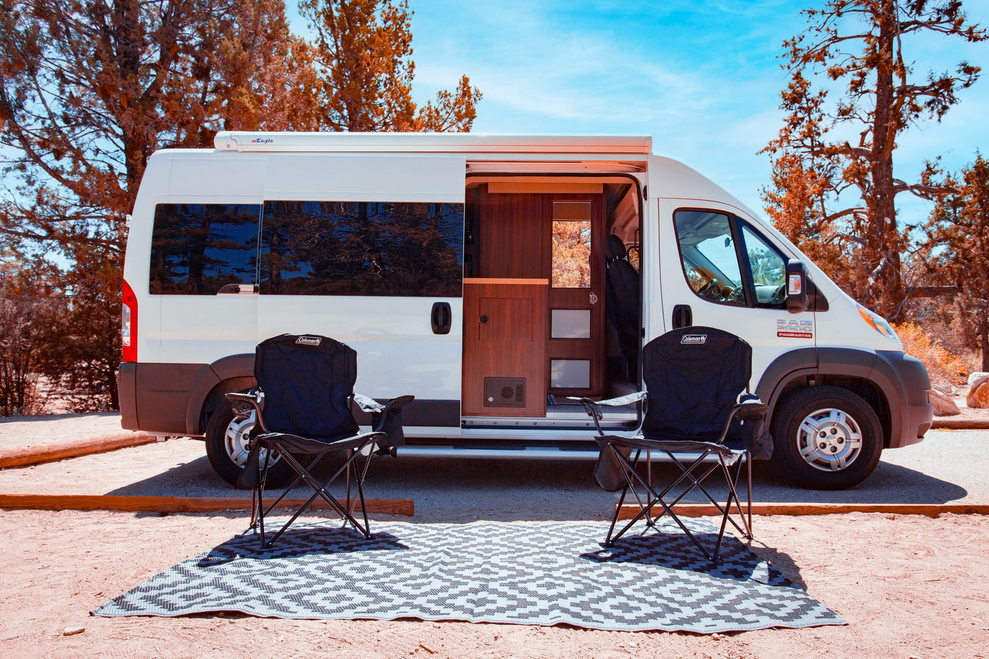  and a view of trees. Features a compact kitchen.|RV rental campervan parked at a scenic campsite with an extended awning — photo 4