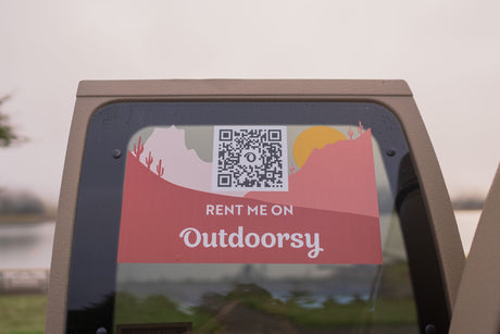 This RV rental sticker on a vehicle's back window displays a QR code to "RENT ME ON Outdoorsy" for your next trip.