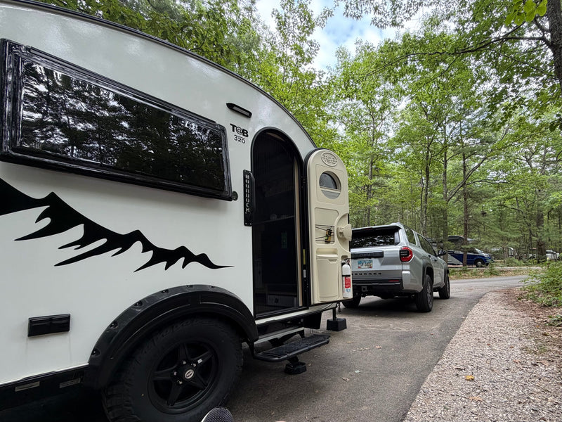  ideal for rv rental adventures. Features off-road tires & mountain graphics.|An rv rental teardrop trailer and SUV parked at a lush — photo 2