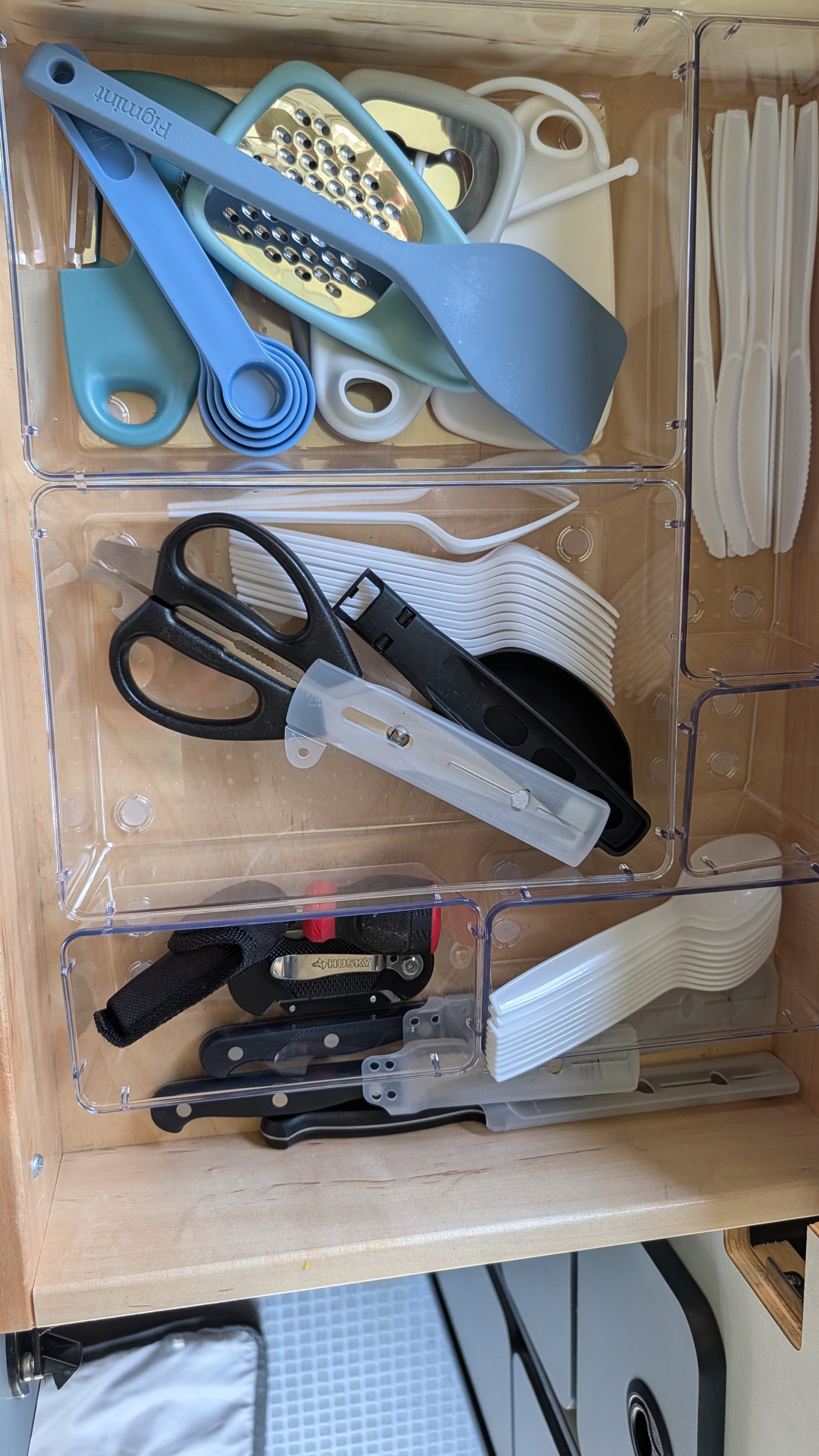 Organized kitchen drawer in an RV rental, showing cooking tools, shears, knives, and disposable cutlery in clear bins.