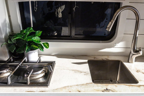 Compact RV rental kitchen with a two-burner stove, unique sink, modern faucet, and potted plants for charm.