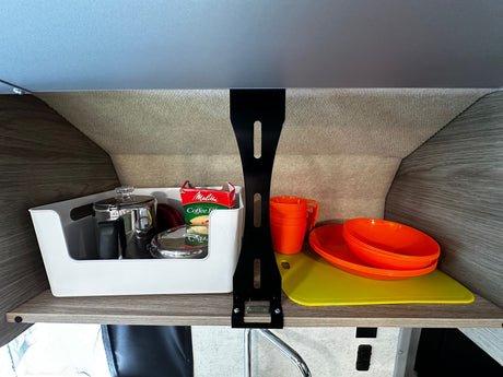 Compact RV rental kitchen storage: coffee essentials, orange dinnerware, & cutting boards neatly stowed on a shelf.