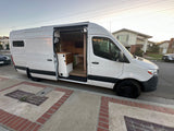 Stylish white camper van conversion with open door revealing a cozy wood interior and kitchen setup, ideal for rv rental.