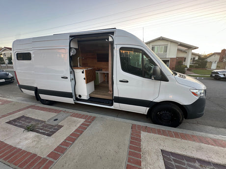 Stylish white camper van conversion with open door revealing a cozy wood interior and kitchen setup, ideal for rv rental.