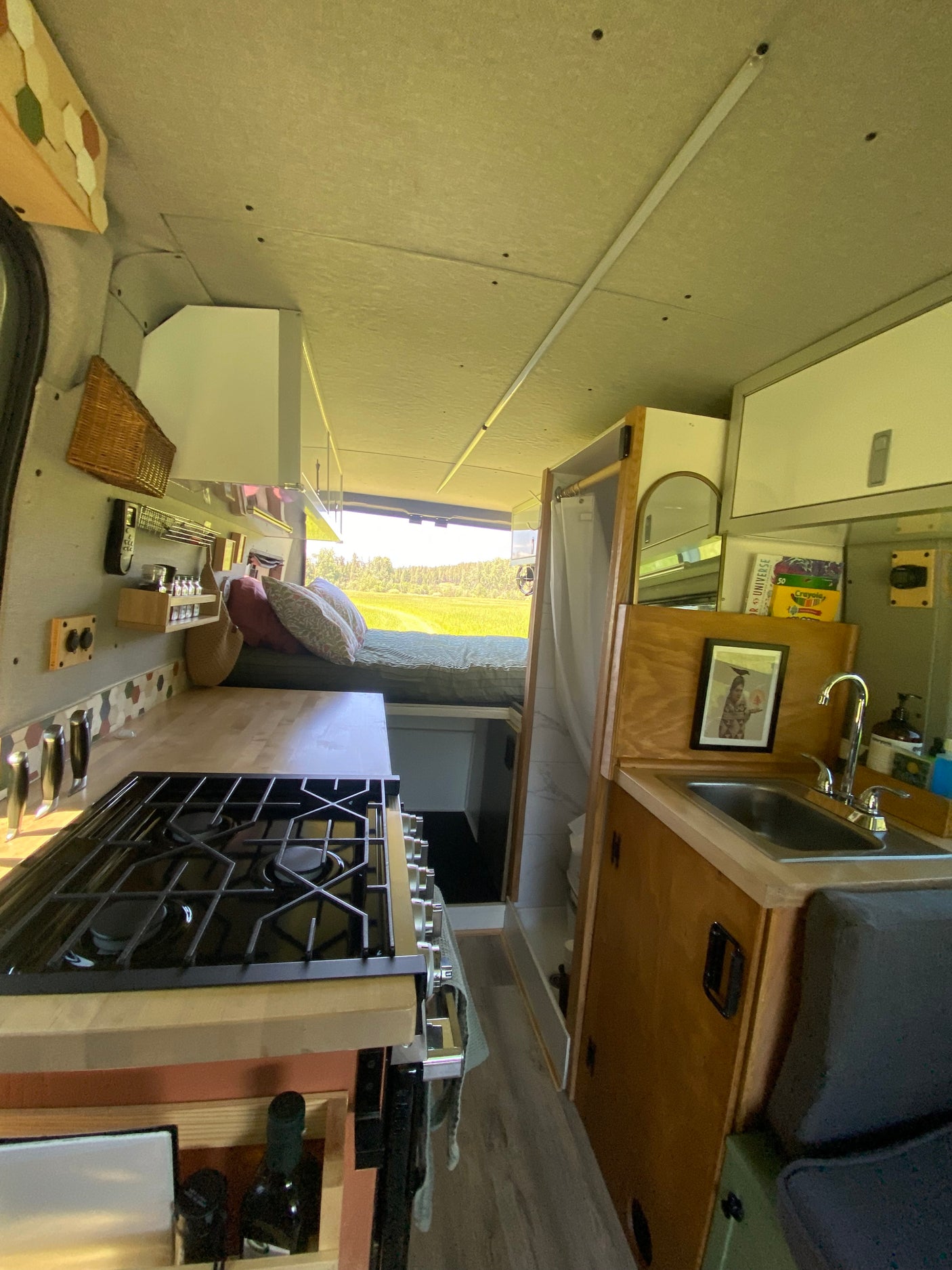 This RV rental's cozy interior features a full kitchen with a stove and sink, a bed with pillows, and a compact shower.