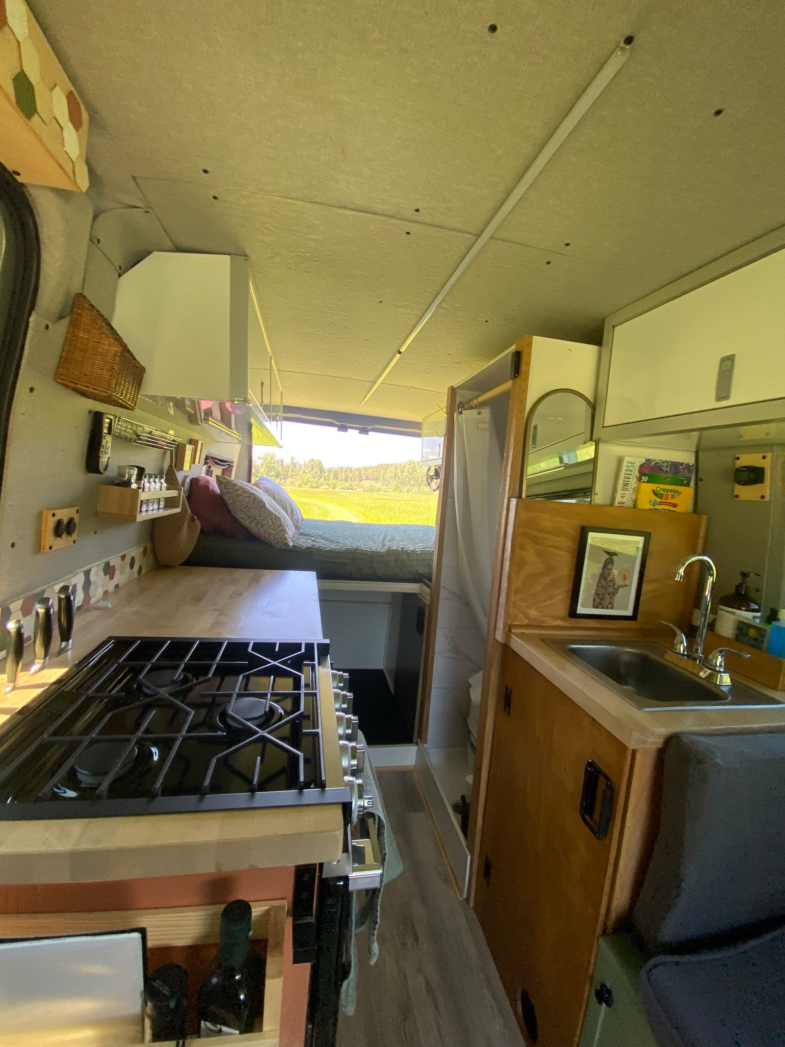 This RV rental's cozy interior features a full kitchen with a stove and sink, a bed with pillows, and a compact shower.