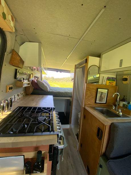 This RV rental's cozy interior features a full kitchen with a stove and sink, a bed with pillows, and a compact shower.