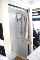 Inside an rv rental: a compact bathroom featuring a shower, toilet, mirror, and towel, perfect for on-the-road convenience.