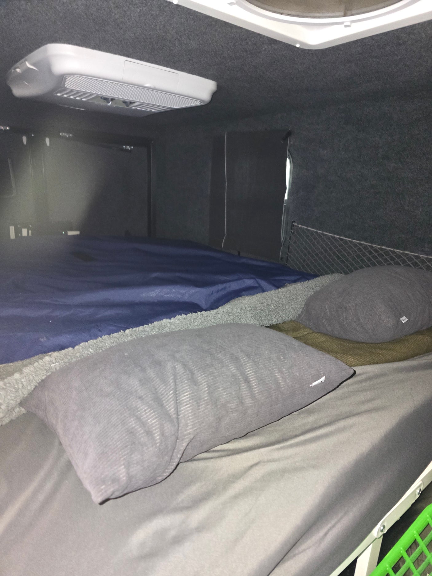 RV rental interior: Cozy sleeping area with grey pillows, blue bedding, and an overhead AC unit for comfortable travel.