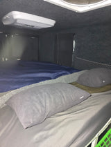RV rental interior: Cozy sleeping area with grey pillows, blue bedding, and an overhead AC unit for comfortable travel.