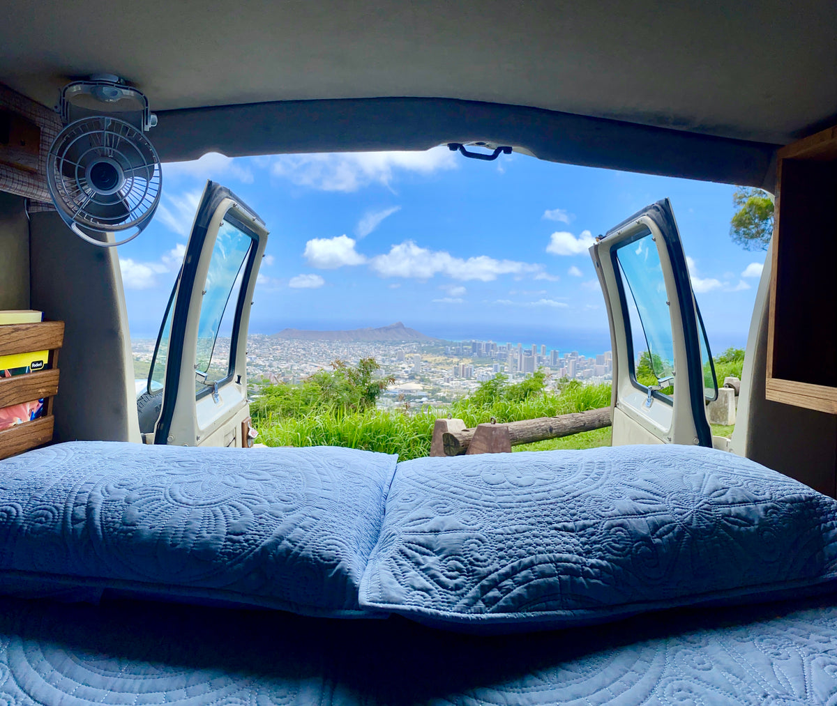 Comfortable RV rental bed with open doors revealing a stunning panoramic city, mountain, and ocean view. — photo 11