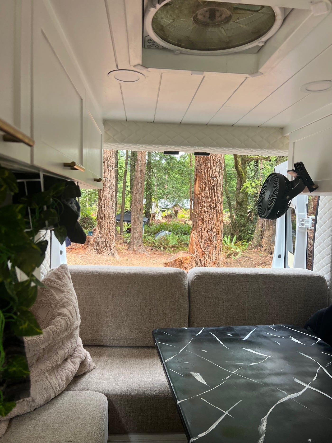 Cozy RV rental interior with gray sofa, black marble table, and a fan, looking out to a serene forest view. — photo 10