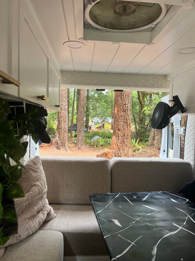 Cozy RV rental interior with gray sofa, black marble table, and a fan, looking out to a serene forest view. — photo 10
