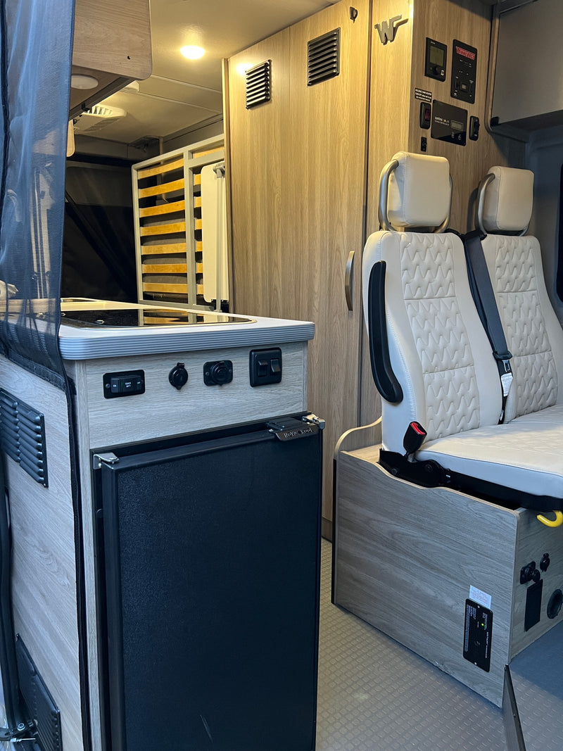 Inside an RV rental: modern camper van interior with kitchen, built-in fridge, two seats, control panel, and rear bed. — photo 16