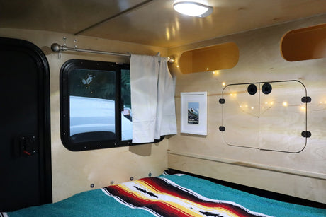 Cozy RV rental interior featuring a bed, window, and charming string lights for your adventure.