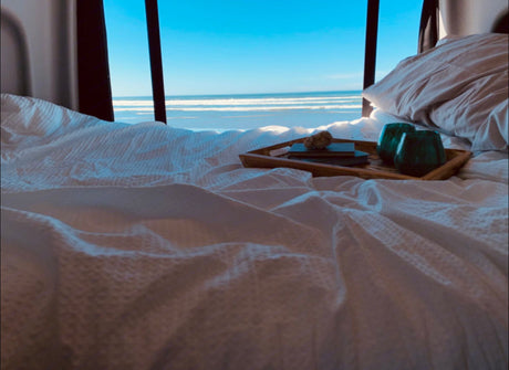 Wake up to ocean views! Comfy bed, tray with drinks & book in this cozy RV rental. Perfect escape.