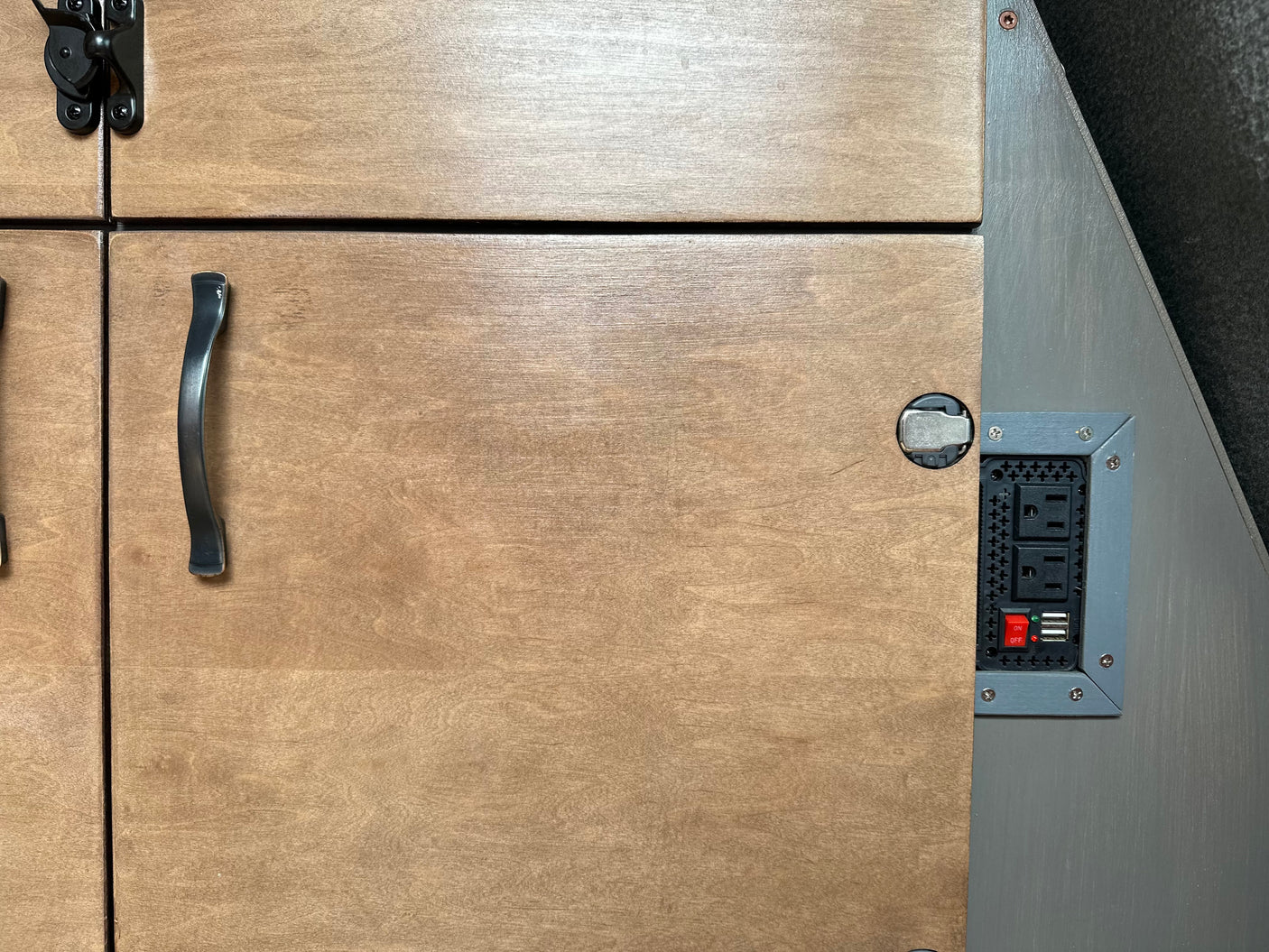 RV rental amenities: Close-up on light wood cabinets, black handle/latch, and a power outlet with USB & ON/OFF switch.