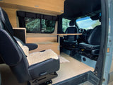 This rv rental camper van's interior showcases swiveling front seats, a wooden table, and built-in cabinetry.