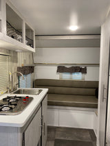 Cozy rv rental interior featuring a compact kitchen with sink, stove, and a versatile sofa/dinette space.