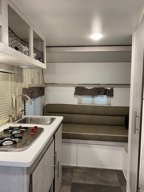 Cozy rv rental interior featuring a compact kitchen with sink, stove, and a versatile sofa/dinette space.
