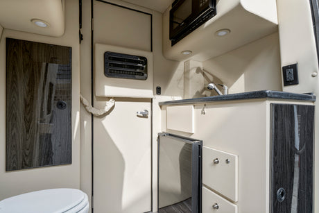 RV rental interior featuring a compact kitchen with microwave, sink, fridge, and a partial view of the bathroom.