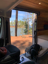 Serene RV rental view: cozy interior, sleeping dog, and a beautiful lakeside camping spot with a fire pit.