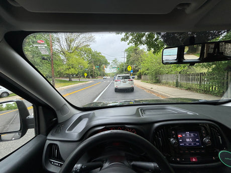 View from a car's driver seat on a tree-lined road. For road trips, an RV rental provides spacious travel options.