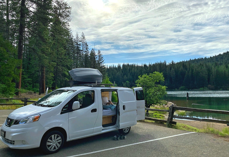 Scenic RV rental camper van by a lake & forest. Its open door reveals a cozy bed, perfect for nature travel. — photo 12
