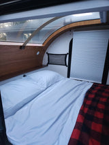 Cozy RV rental interior with a comfortable bed, white sheets, and a red plaid blanket, ready for your adventure.